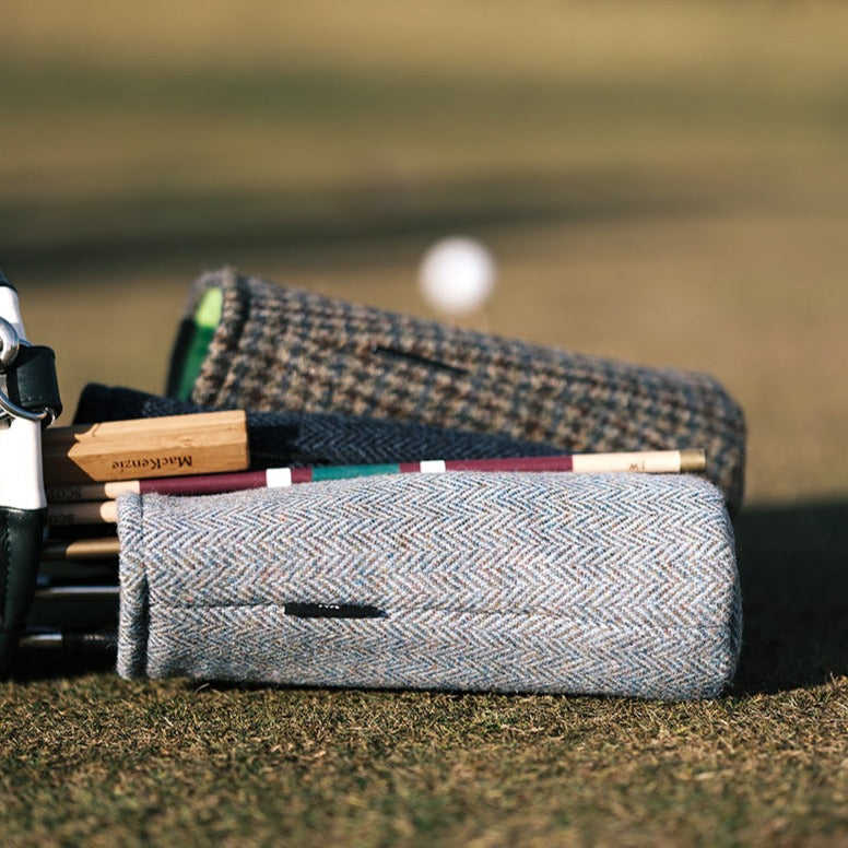 Harris Tweed driver cover in light blue/grey herringbone – A close-up image of a Harris Tweed driver cover featuring a light blue/grey herringbone pattern, highlighting the luxurious texture and craftsmanship of the cover, set in a natural outdoor golf course setting.