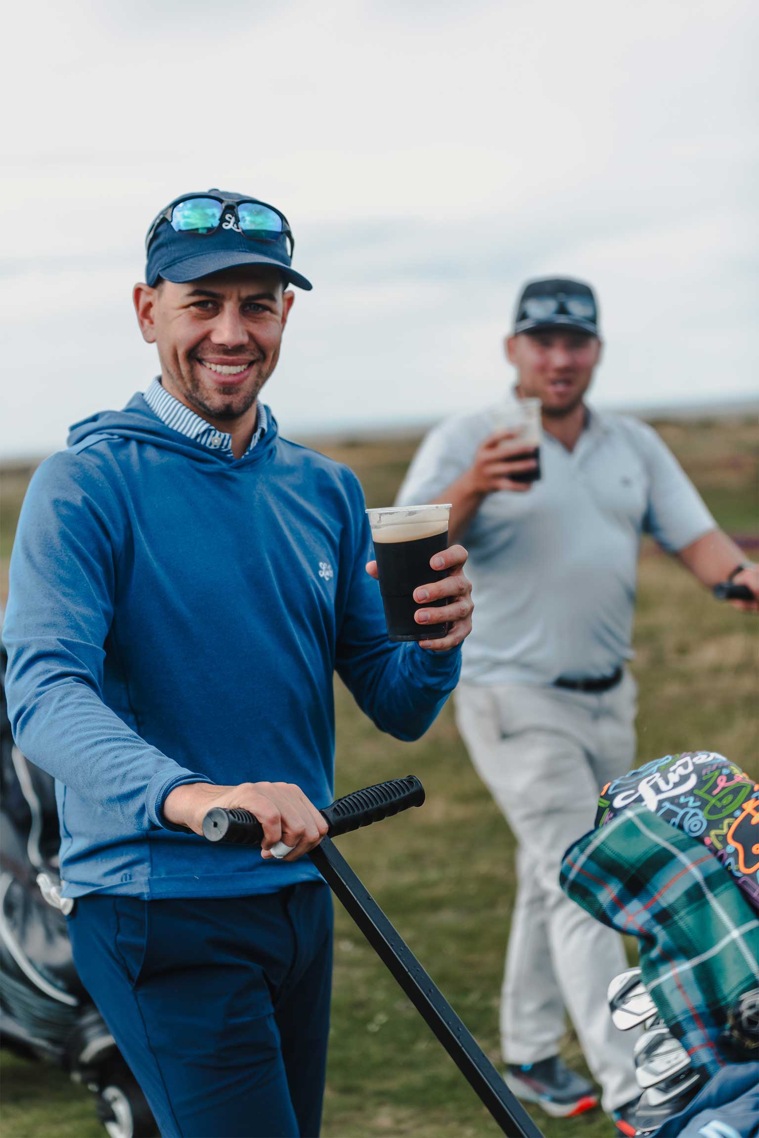 Two golfers drinking a Guiness pint on the golf course: A photo taken during a golf day at Spey Bay event for Links Golf. A Fyfe Tartan headcover is shown in the image.