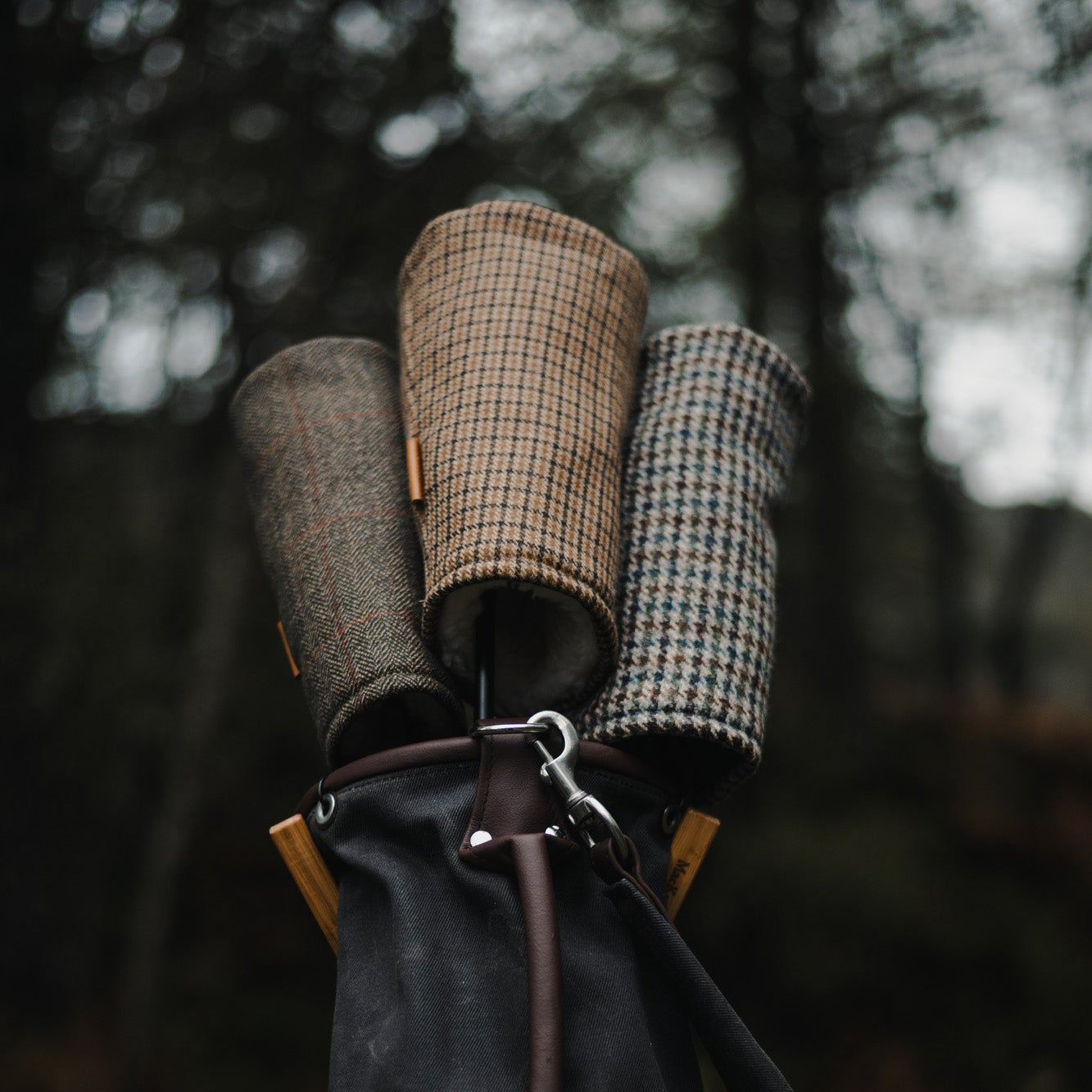 Black bag with plaid and checkered golf headcover against a blurred natural background